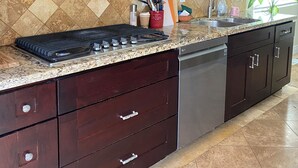 Una cocina con alacenas de madera oscura, campana extractora de acero inoxidable, encimeras de granito y lavavajillas.