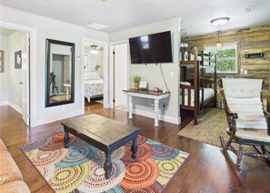 Un salon avec une table basse en bois, un tapis coloré, un téléviseur et un fauteuil à bascule.