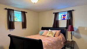 Une chambre à coucher avec un lit, une table de chevet, une lampe et une fenêtre avec des rideaux.