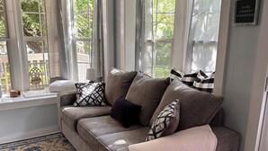 A cozy living room with a grey sofa, patterned rugs, and large windows with curtains. - Cici's Guest House Top rated stay in Laurel (Laurel)