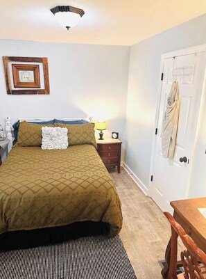 A bedroom with a bed, a nightstand, a lamp, a framed picture, and a door. - Cici's Guest House Top rated stay in Laurel (Laurel)