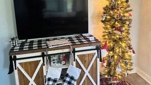 A living room with a TV, a Christmas tree, and a checkered table with boots. - Cici's Guest House Top rated stay in Laurel (Laurel)