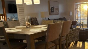 Ruokailutila, jossa on puinen pöytä ja tuolit, koristeellinen pöytäkoriste ja suuri ikkuna, josta tulee runsaasti luonnonvaloa.