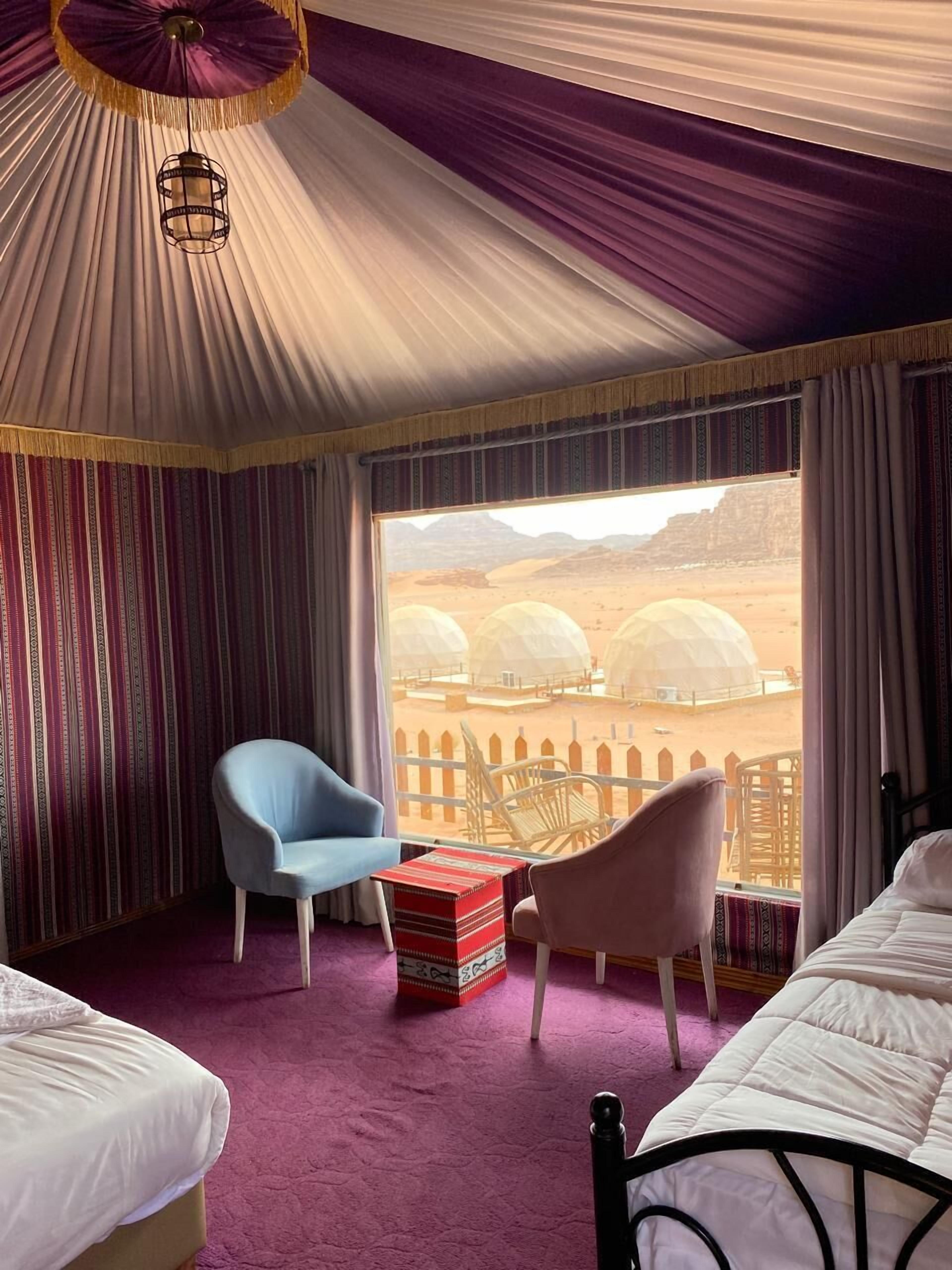 Une chambre avec un lit, deux chaises, une petite table et une vue sur les tentes du désert.