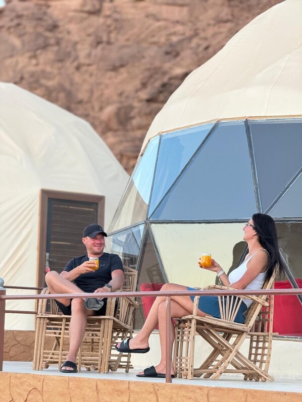 Two people sitting on wicker chairs outside a geodesic dome structure, likely a part of a resort or vacation rental. - Whispers of the Stars Luxury Camp  (Wadi Rum)