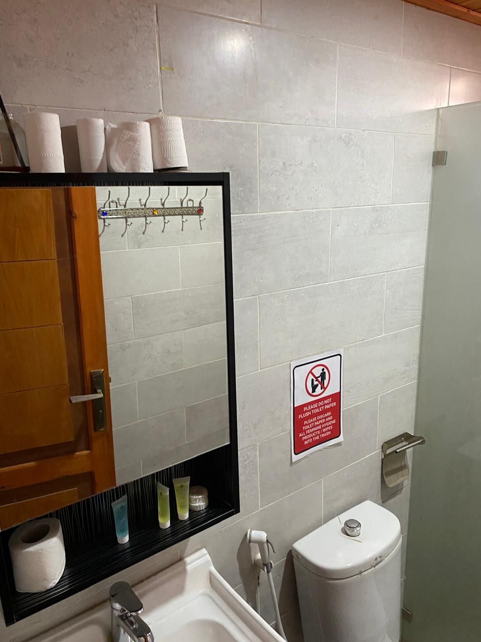 A bathroom with a mirror, toilet, sink, and a sign prohibiting flushing toilet paper.