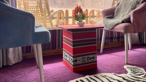 Una habitación con vistas a una cordillera, un reposapiés rojo con estampado, dos sillas de mimbre y una alfombra púrpura.