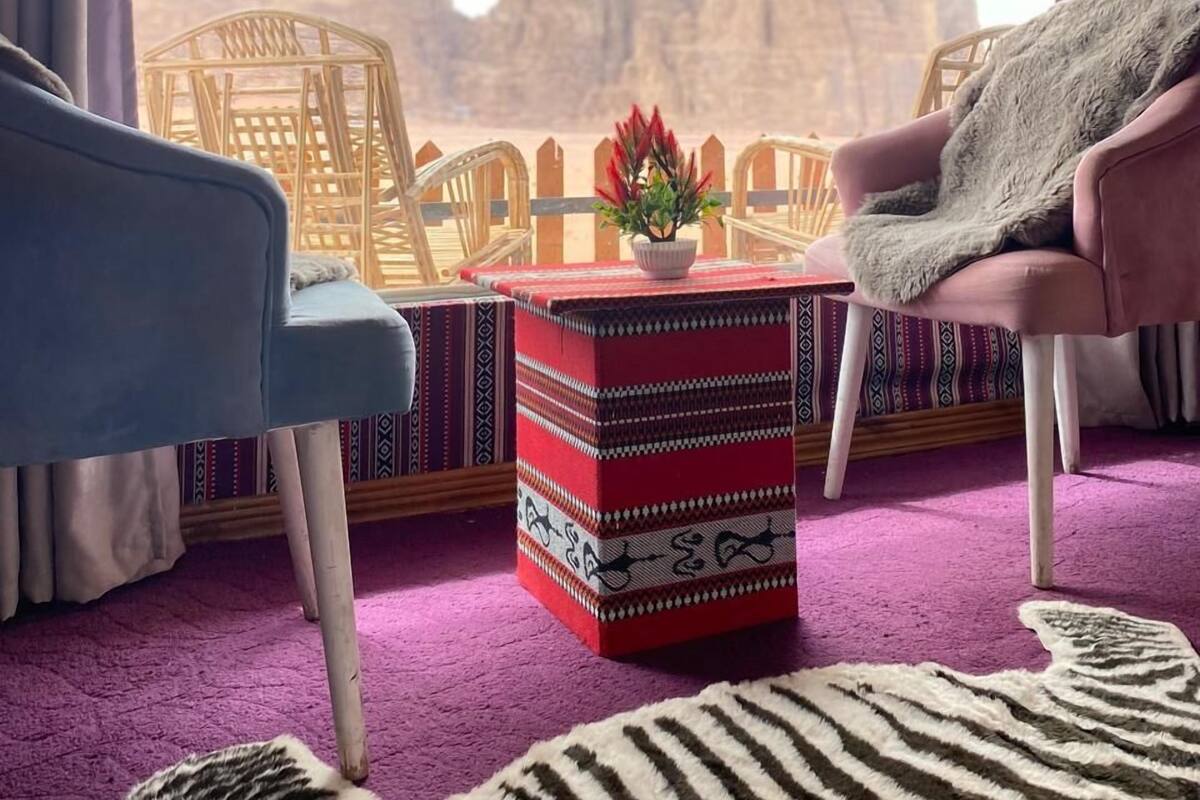 Una habitación con vistas a una cordillera, un reposapiés rojo con estampado, dos sillas de mimbre y una alfombra púrpura.