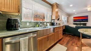 Una cocina moderna con lavavajillas de acero inoxidable, armarios de madera, un amplio ventanal y un cuadro de paisaje urbano en la pared.