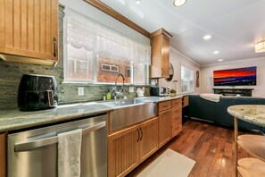 A modern kitchen with a stainless steel dishwasher, wooden cabinets, a large window, and a cityscape painting on the wall. - Tahoe Keys Cozy Mountain Retreat 3BR, 3BA (South Lake Tahoe)