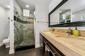 A modern bathroom with a marble shower enclosure, a wooden vanity with a sink, and a large mirror.