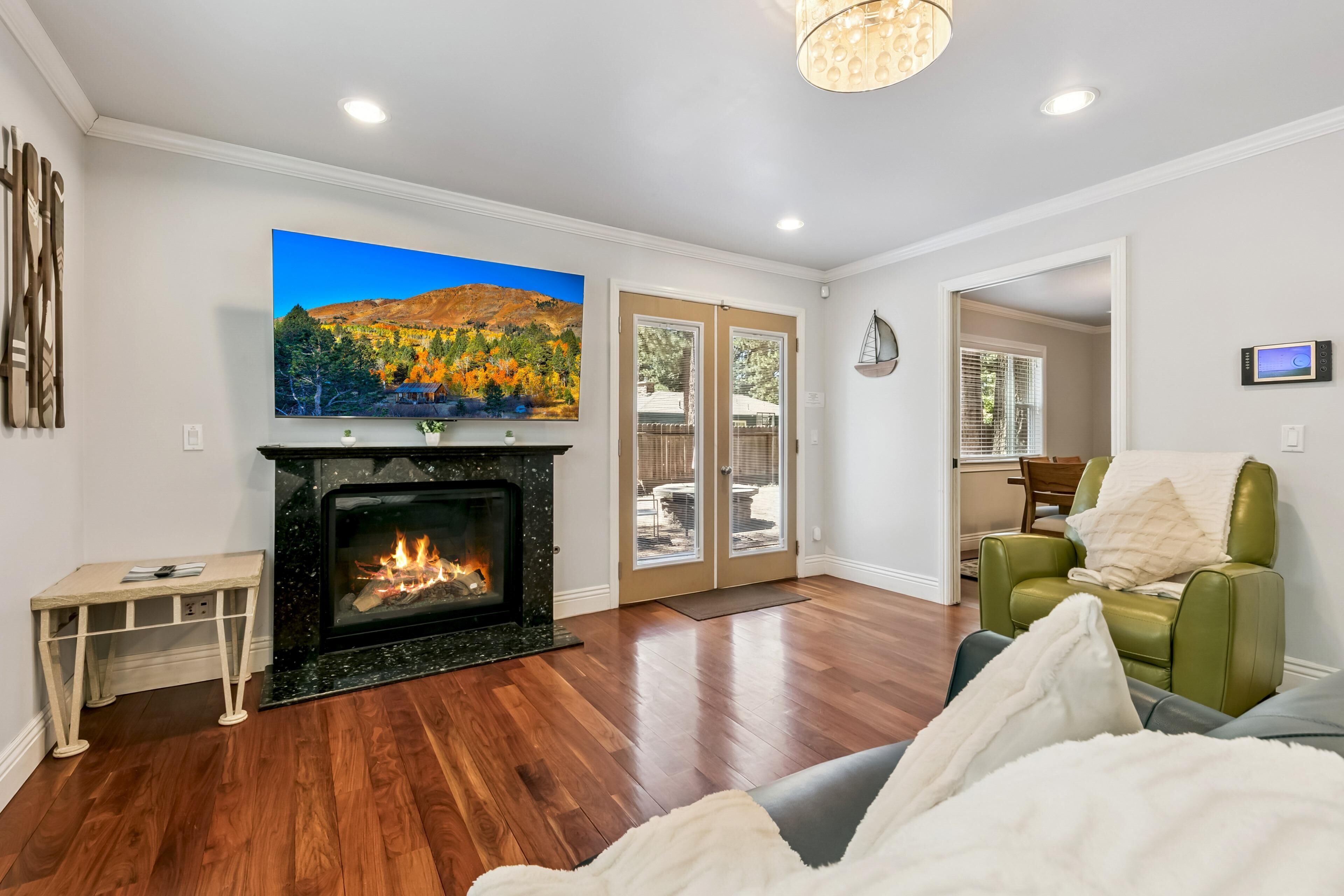 A living room with hardwood flooring, a fireplace, a television mounted above it, and a green armchair.
