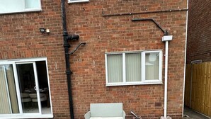 Une maison en briques dotée d’un patio comprenant un ensemble de mobilier d’extérieur blanc et une porte-fenêtre coulissante donnant sur une pièce.