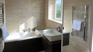 Une salle de bain moderne avec une baignoire, un grand miroir et une fenêtre.