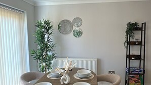 Un coin repas avec une table ronde dressée pour six personnes, un radiateur, une plante et une bibliothèque.