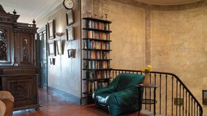 Una biblioteca con un sillón de cuero verde, estanterías y un reloj en la pared.