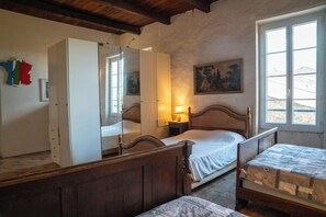 A bedroom with a wooden bed, a bedside table with a lamp, a window with a view, and a mirror on the wall.