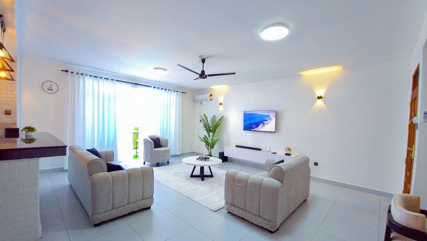 A modern living room with two sofas, a coffee table, a TV, and a ceiling fan.