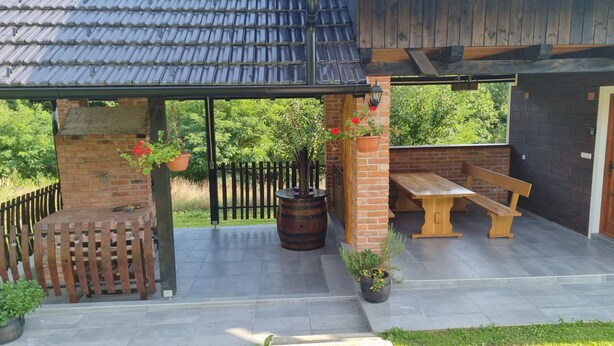 Un patio couvert avec un banc en bois et une table, entouré de plantes en pot et d’un mur en briques.