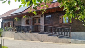 Une maison en bois avec des fondations en pierre, un balcon doté d’une rambarde en métal et des panneaux solaires sur le toit.