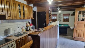 Une cuisine avec des meubles en bois, un four encastré, un évier et, au fond, une table de billard.