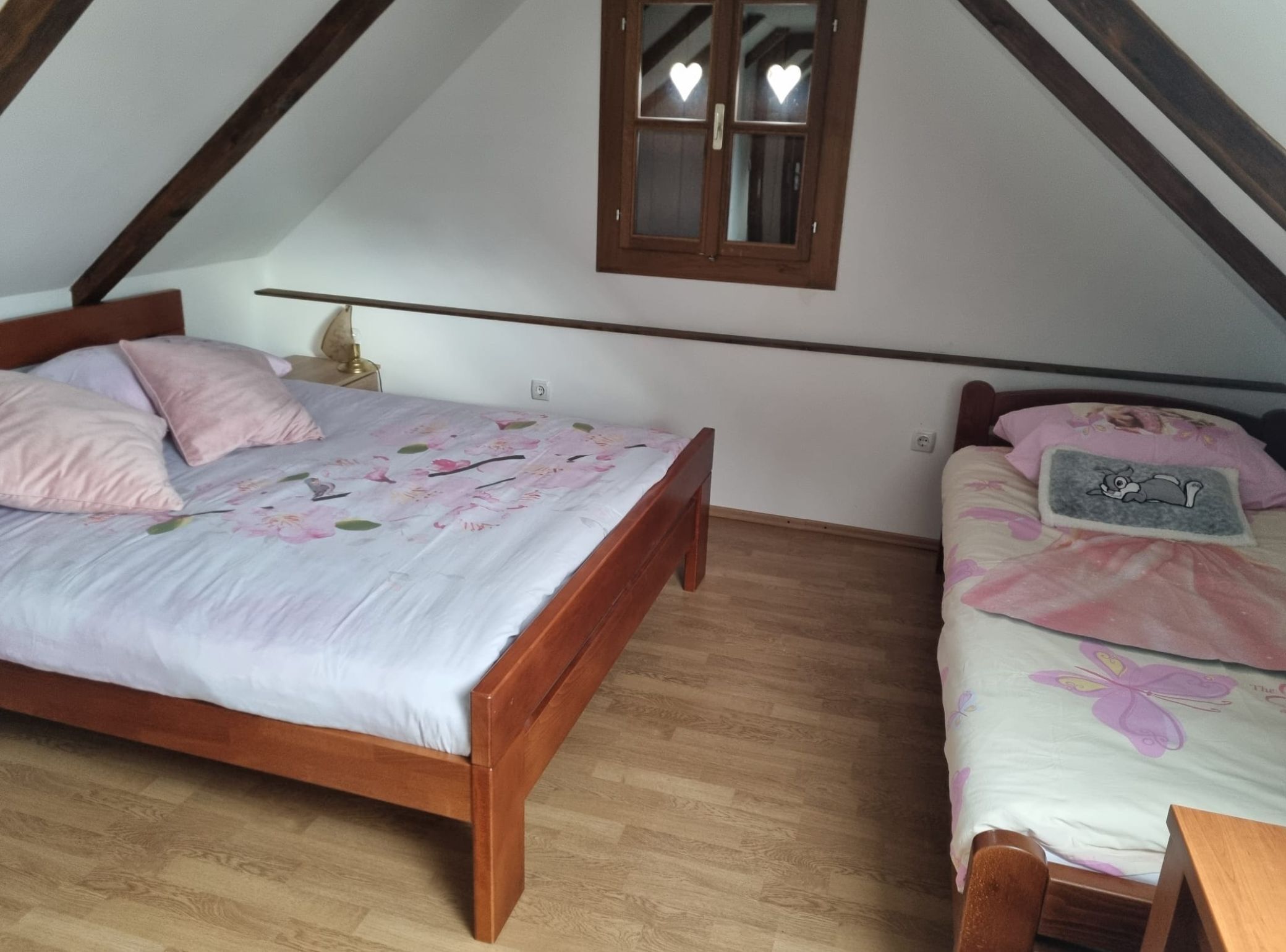 A bedroom with two wooden beds, a window with heart-shaped decorations, and a wooden floor.