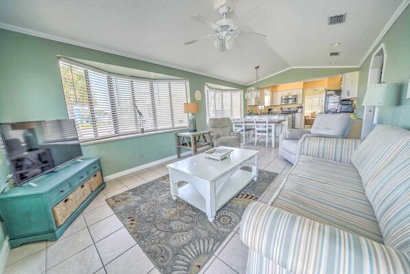 A living room with a TV, sofa, coffee table, and a dining area with chairs and a table.