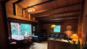 A cozy cabin interior with a dining area, a sofa, a television, and a clock on the wall. - Pure Nature – House with a Large Garden by the Forest (Langendorf)