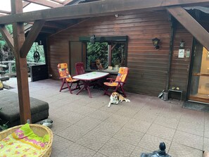 Un patio al aire libre con una mesa y sillas de madera, un perro y una cesta de mimbre.