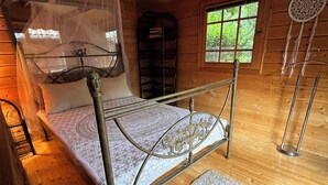 A wooden cabin bedroom with a metal bed frame, a canopy bed, a small window, and a dreamcatcher. - Pure Nature – House with a Large Garden by the Forest (Langendorf)