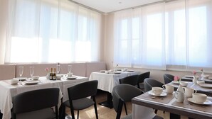 A dining area with tables set for four, each with white tablecloths, black chairs, and a variety of tableware. - Raya Hotel (Mediglia)