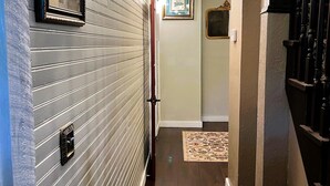 A hallway with a wooden floor, a chandelier, and a door with a black frame.