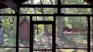 A rustic cabin with a wooden door and windows, surrounded by a forested area.