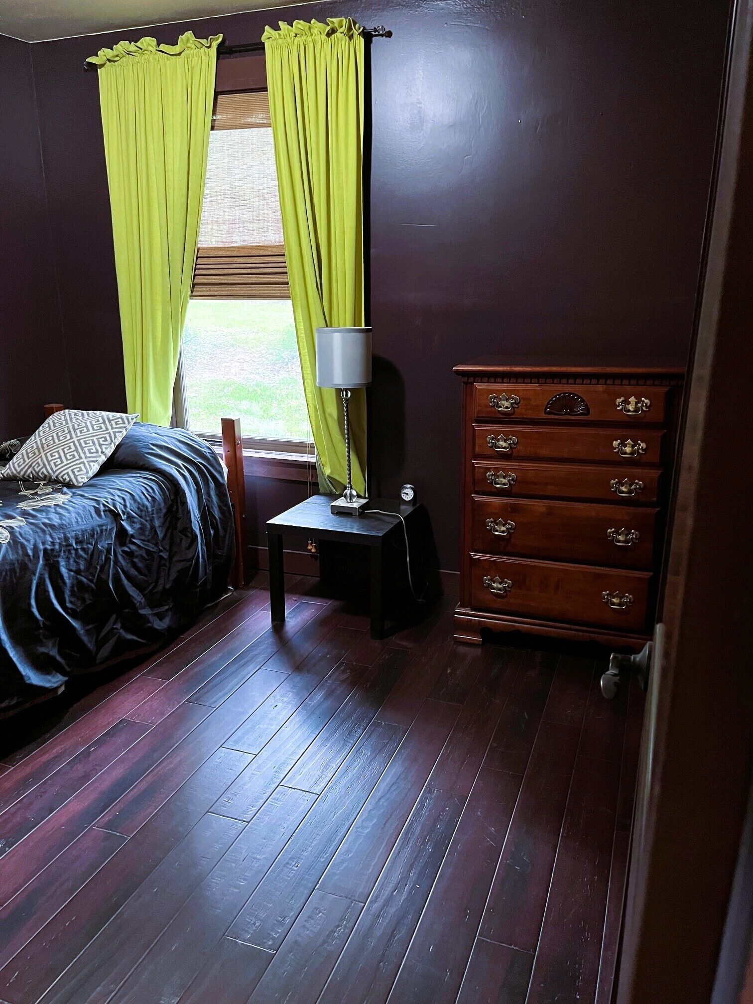 A bedroom with a bed, a dresser, a lamp, and a window with curtains.
