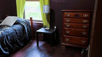 A bedroom with a bed, a dresser, a lamp, and a window with curtains.
