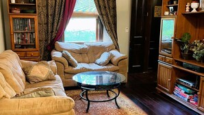A living room with a beige sofa, a glass coffee table, a patterned rug, a bookshelf, and a television.