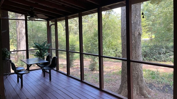 A covered outdoor seating area with a table and chairs, large windows, and a ceiling fan.