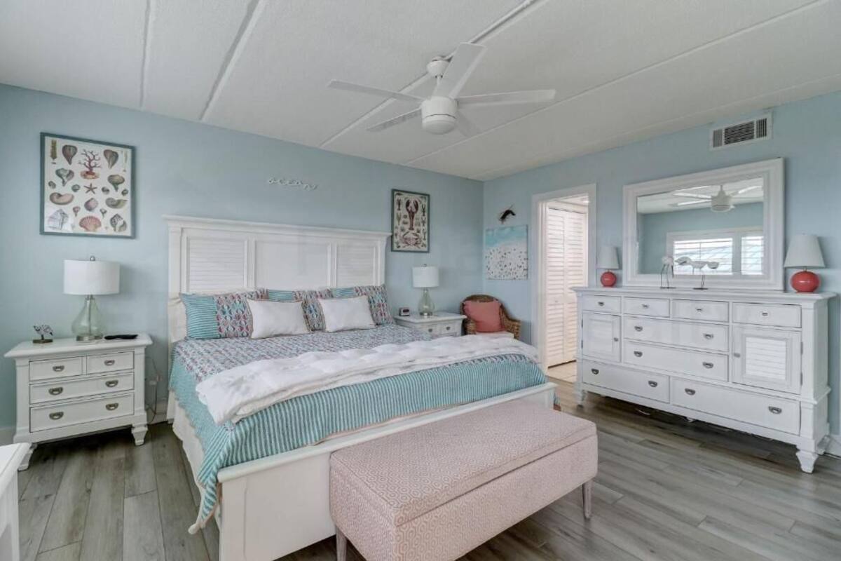 Une chambre à coucher comprenant un lit, des tables de chevet, une commode et un ventilateur de plafond.