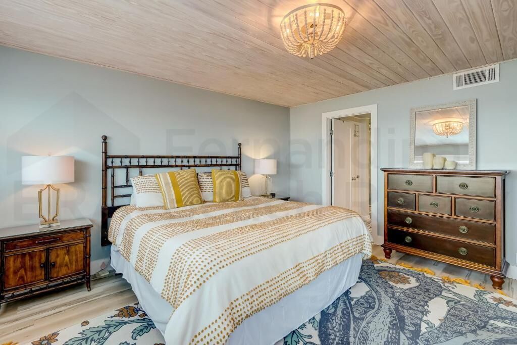 A bedroom with a wooden bed, two bedside tables with lamps, a dresser, and a chandelier.