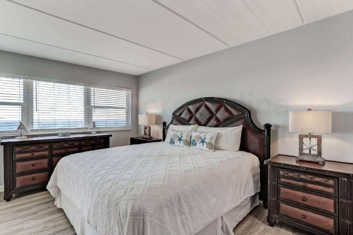 Une chambre à coucher avec un grand lit, une commode, une table de chevet et une fenêtre avec des stores.