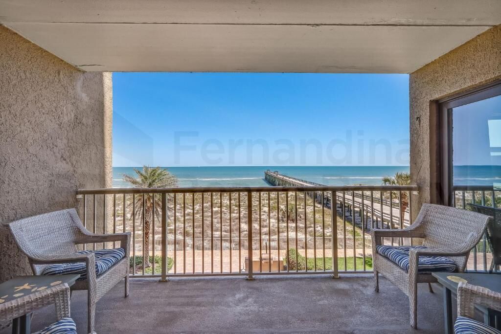 A balcony with wicker furniture, a view of the beach, and a pier.