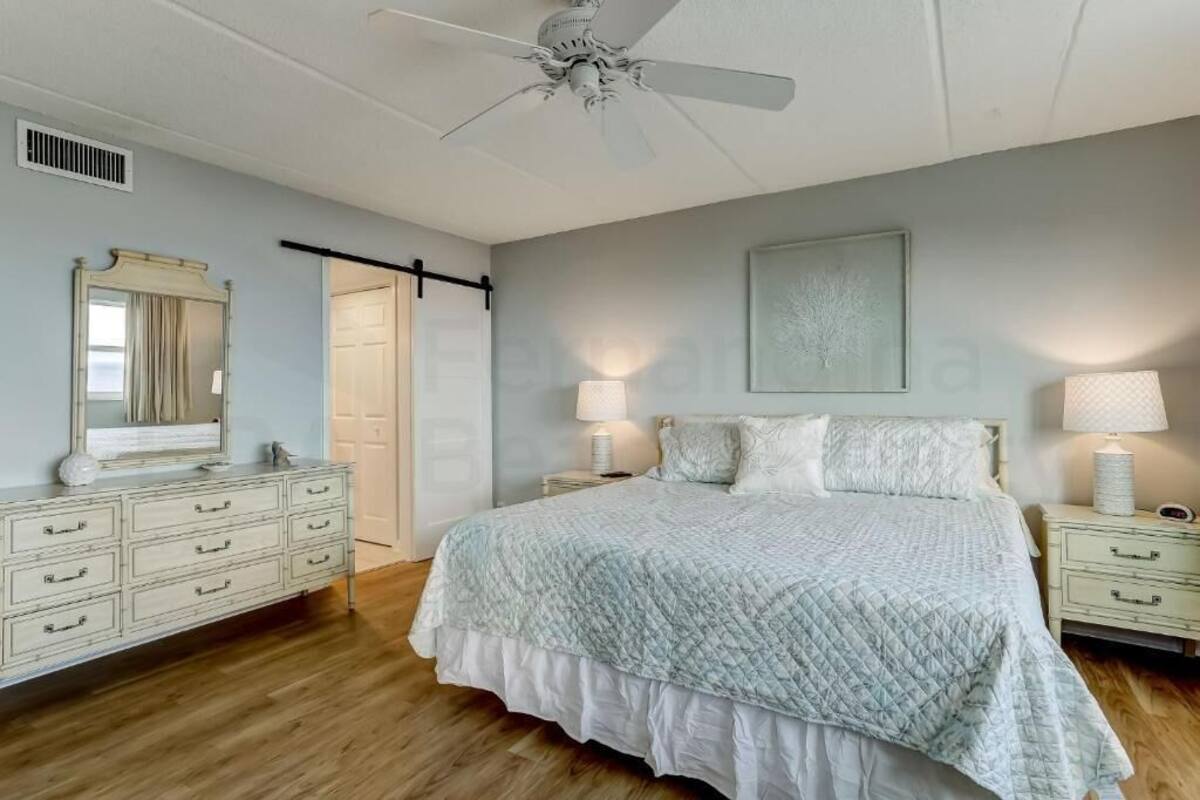 Une chambre à coucher avec un lit, des lampes de chevet, une commode, un ventilateur de plafond et une porte.