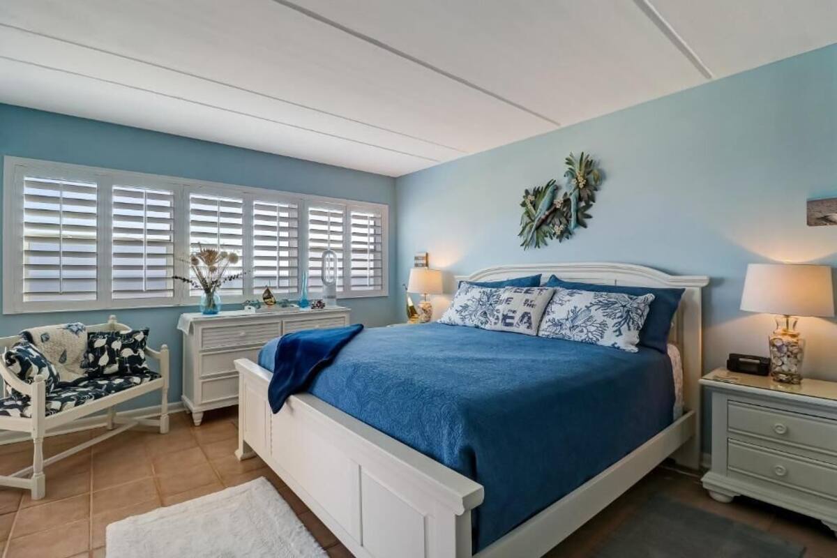 Une chambre à coucher avec un lit, des tables de chevet, une commode et une fenêtre avec des volets.