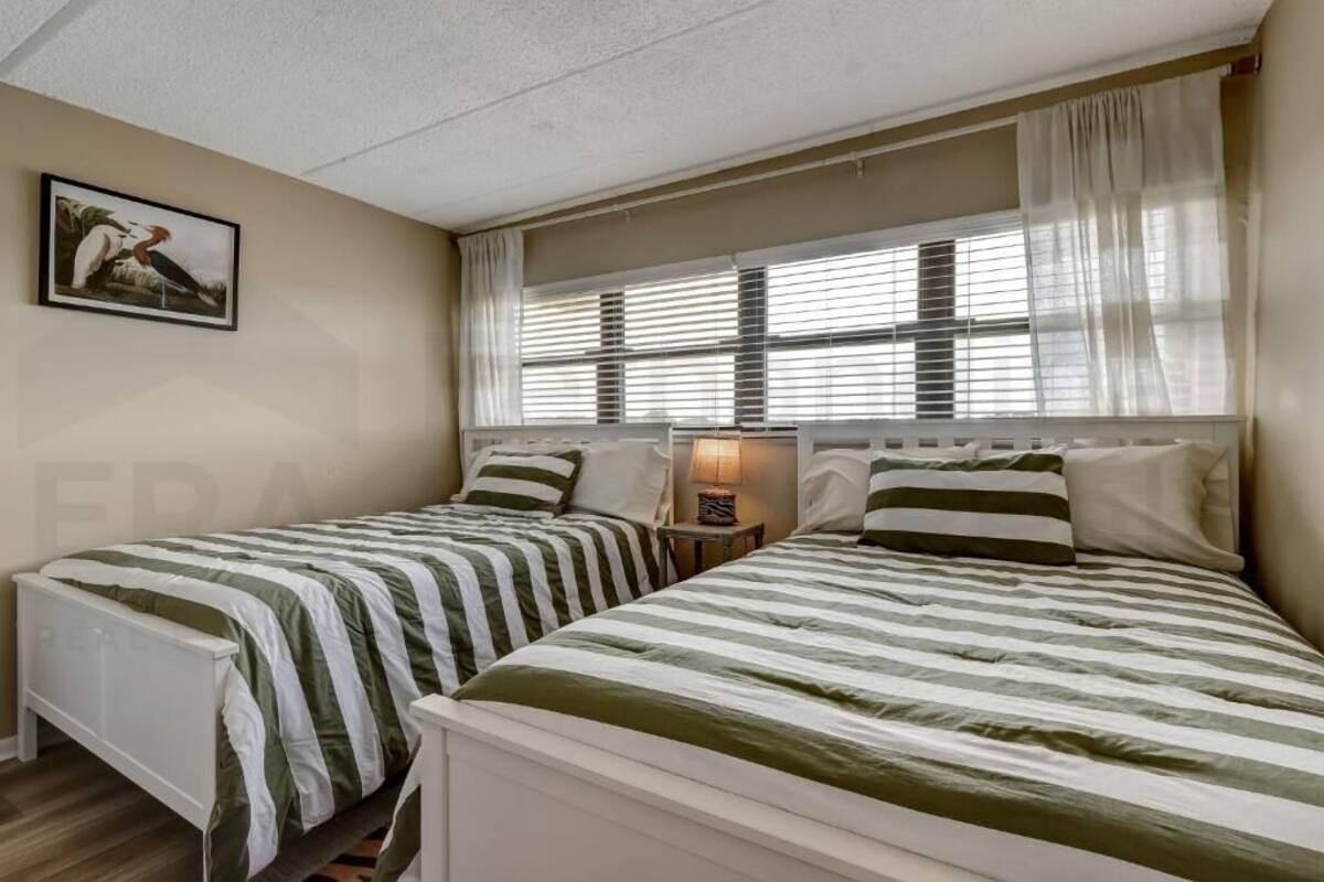 Une chambre avec deux lits, une table de chevet, une lampe et une fenêtre avec des rideaux.