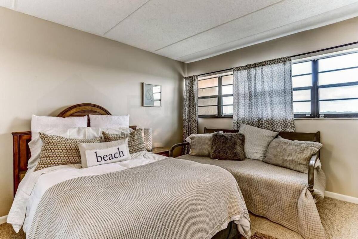 Une chambre avec deux lits, une fenêtre ornée de rideaux à motifs et un tableau accroché au mur.
