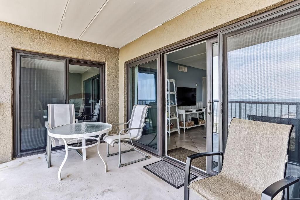 A balcony with a glass door leading to a room, a round table, and two chairs.