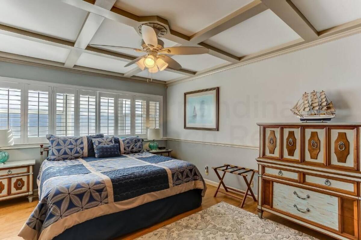 Une chambre avec un grand lit, un ventilateur de plafond, une commode et une maquette de bateau posée sur le dessus.