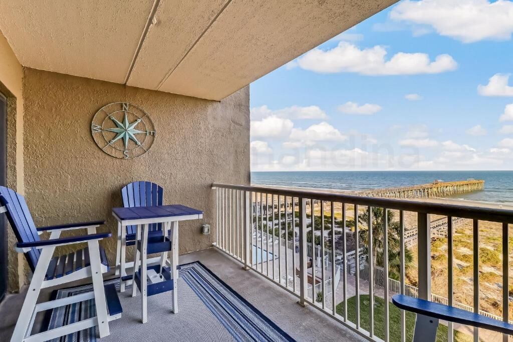 A balcony with a view of the ocean, a pier, and a compass decoration on the wall.