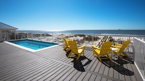 A wooden deck with a pool and yellow chairs overlooking the beach.