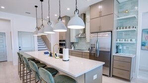 A modern kitchen with a central island, bar stools, stainless steel appliances, and pendant lighting.